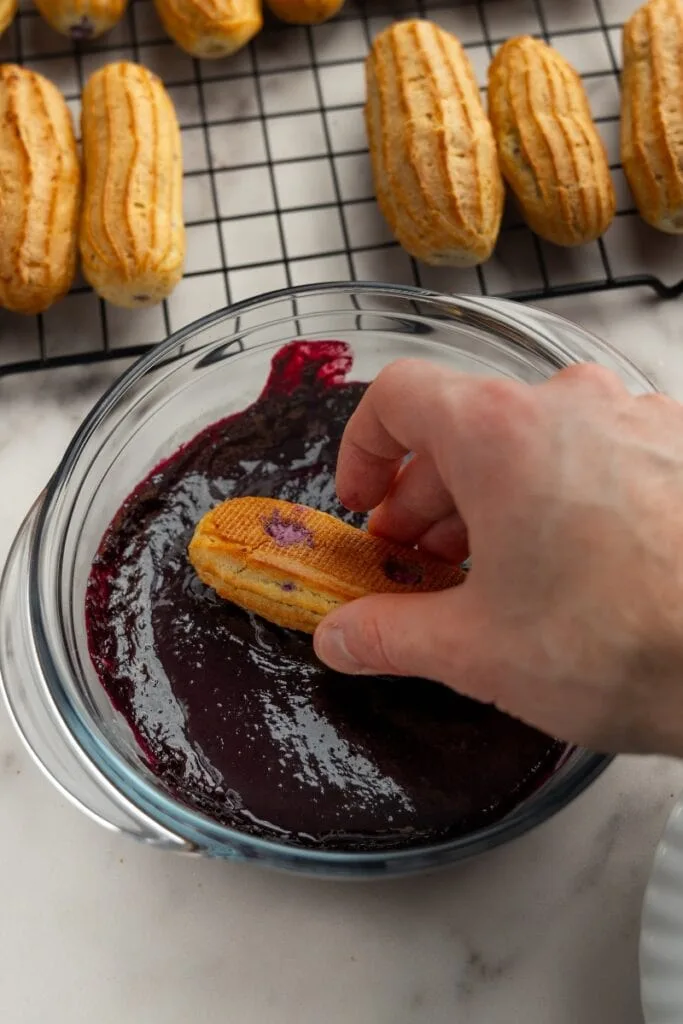 Dipping the top of the eclair in blueberry ganache
