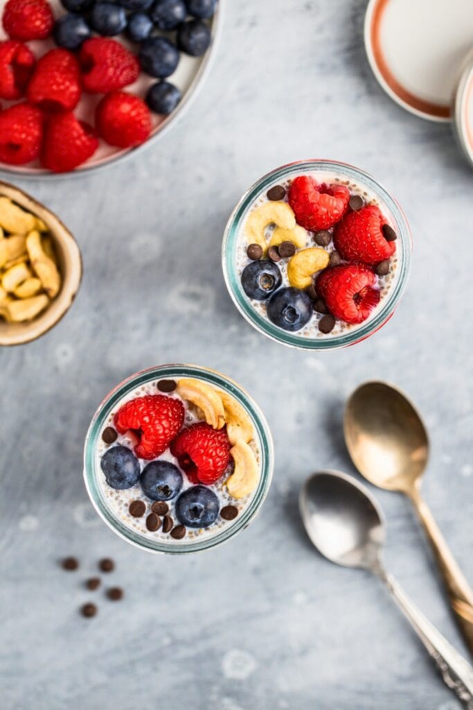Two jars of chia pudding topped with berries cashews and chocolate chips