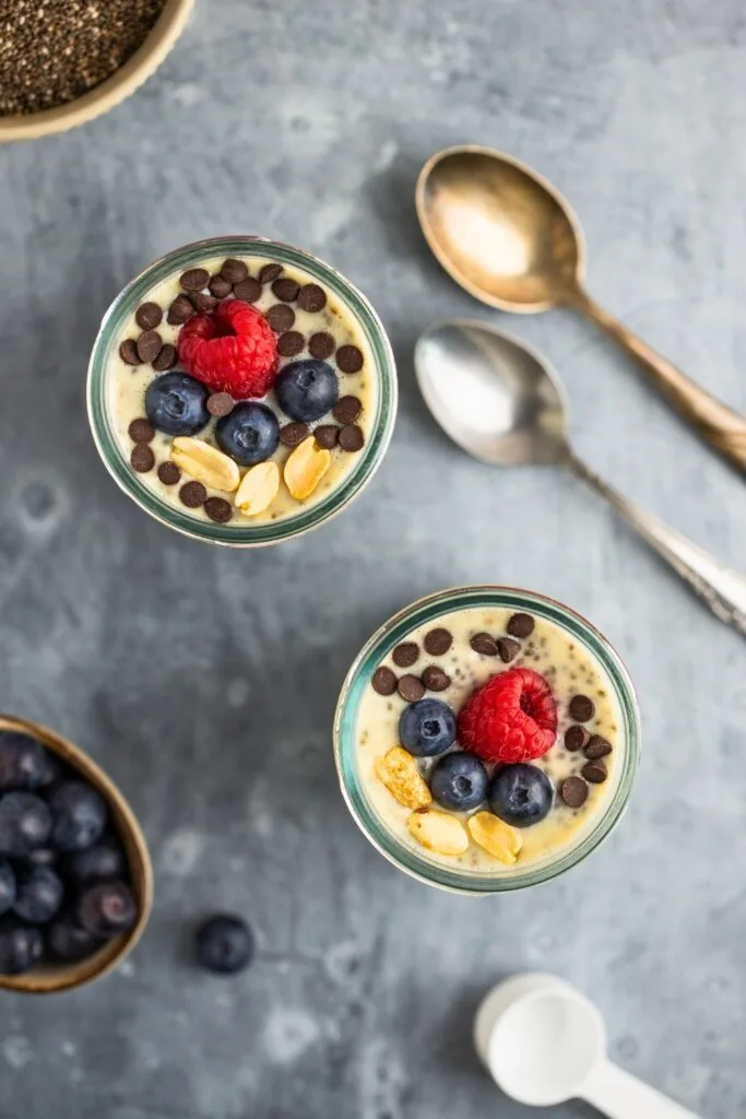Glass jars filled with protein powder chia pudding with berries nuts and chocolate chips topping