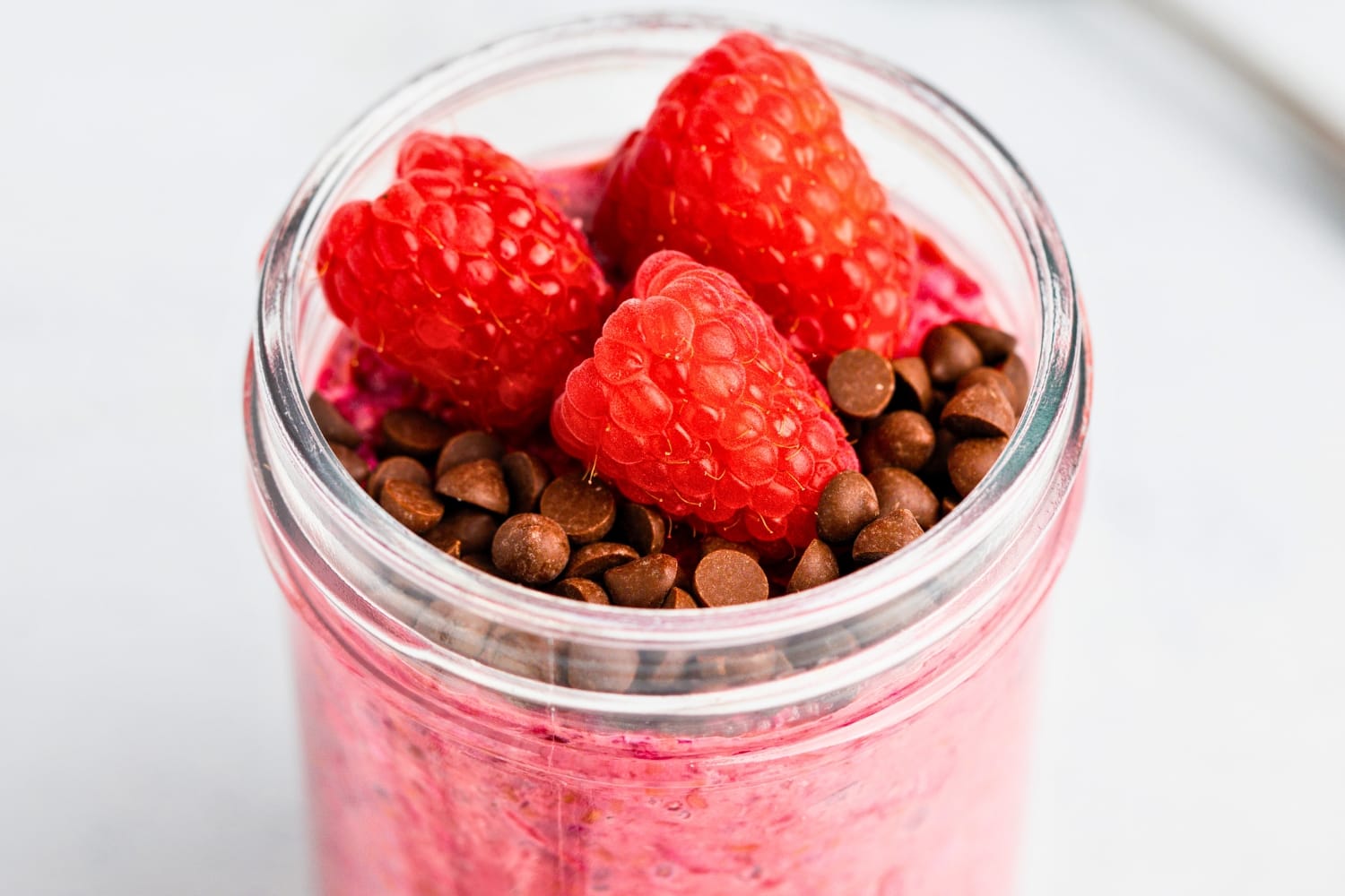 Chilled glass jar of raspberry overnight oats with berries and chocolate