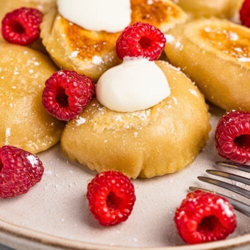 Apple filled pierogi served with a topping and fresh raspberries