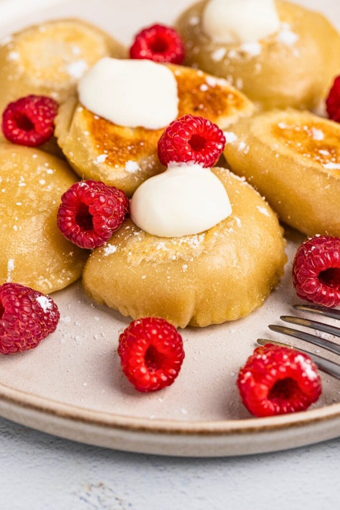 Apple filled pierogi served with a topping and fresh raspberries